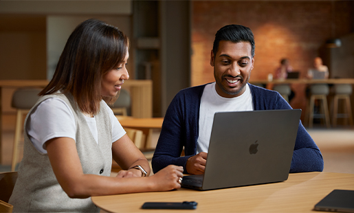 عمار يتعاون مع زميلة له أثناء الجلوس أمام جهاز MacBook على طاولة في منطقة مشتركة.